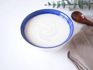 Homemade greek yogurt or sour cream in blue bowl with wooden spoon and fabric or napkin over white wooden background. Food helps the digestive system..