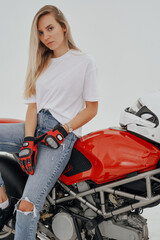 Obraz na płótnie Canvas Studio shot of active woman with long blond hairs riding red motorbike against white background.