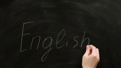 English school. Foreign language study. Female teacher hand writing word on black chalkboard.