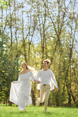 Fototapeta premium Happy newlyweds holding hands and running across the lawn