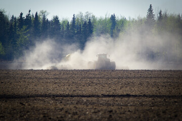 Tractor is seeding in the cloud of dust in spring, agricultural field.