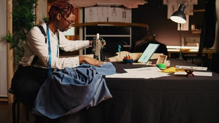 Seamstress using sewing machine to design and craft fashion items at workstation. Professional tailor working with handcraft equipment and tools, creating tailored custom made clothes.