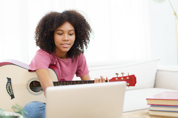Happy cheerful American - African black woman sitting on a sofa in living room and playing an...