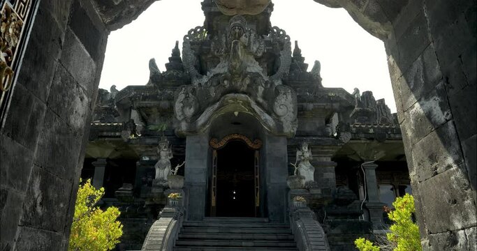 Slow tracking shot unveiling the grandeur of the Bajra Sandhi Monument in Denpasar, Bali, through an impressively adorned golden entrance gate amidst stunning architectural elements