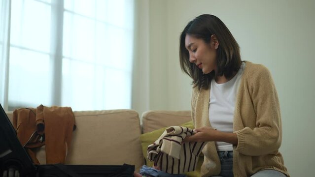 Beautiful woman feeling happy to folding her clothes and pack suitcase for travel in holiday. Young female have a happy feeling folding clothes while packing luggage at home.