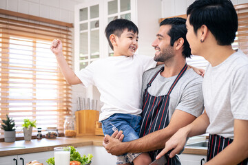 Gay fathers and adopted son enjoying after cooking in the kitchen. Diversity of LGBT relationships. A gay couple and adopted living together concept.