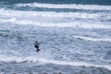 A man kitesurfing on a beach with rough seas 