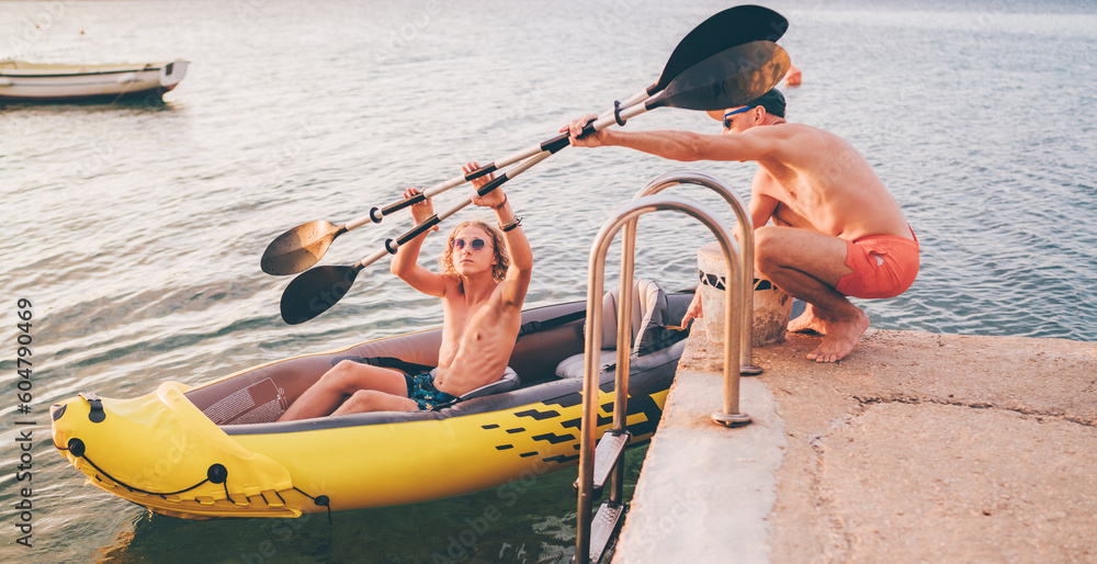 Wall mural father with teenager son preparing evening ride loading oars in an inflatable kayak. adriatic sea ha