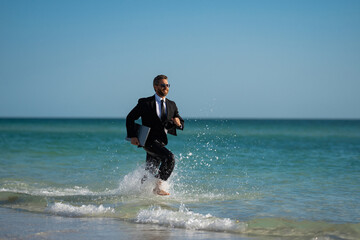 Freelance work, online business. Summer business. Businessman in suit hold laptop and run on sea. Funny business man in a business suit jump with laptop in sea water. Remote work. Crazy freelancer.