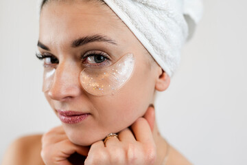 young satisfied caucasian woman in towel applying  hydrogel patches under eyes on face isolated on white