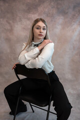 Obraz na płótnie Canvas Pretty woman wear white blouse and black pants sitting on chair and looking at camera, studio shoot