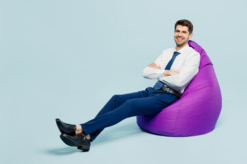 Full body young employee IT business man corporate lawyer wearing classic formal shirt tie work in office sit in bag chair hold hands crossed folded isolated on plain blue background studio portrait.