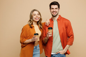 Young couple two friends family man woman wear casual clothes together hold takeaway delivery craft paper brown cup coffee to go isolated on pastel plain light beige color background studio portrait.