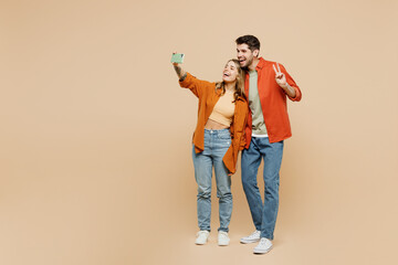 Full body young couple two friends family man woman wear casual clothes together do selfie shot on mobile cell phone post photo on social network isolated on pastel plain light beige color background.