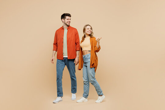 Full body young couple two friends family man woman wear casual clothes together point thumb finger aside indicate on workspace area copy space mock up isolated on pastel plain beige color background.