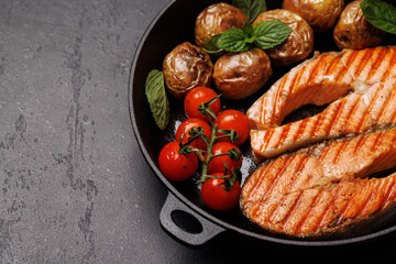 Grilled salmon steaks and potatoes sizzling in a frying pan