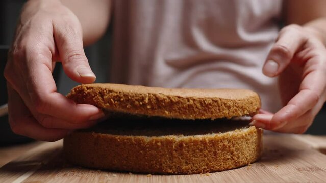 The woman is dividing the sponge cake layer for the cake into two halves and showing the texture inside.