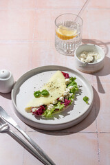French vegetarian omelet filled with feta cheese and green salad for breakfast on pink tile background with clear shadows in hard light, menu