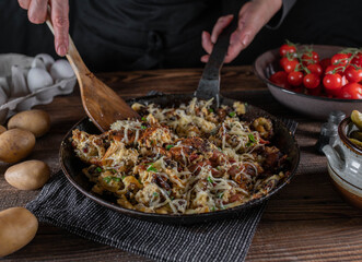 Farmers breakfast with fried potatoes, bacon, eggs, chives, and cheese. Served in a rustic iron pan on wooden table.