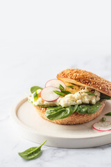Breakfast burger with scrambled eggs, spinach, radish slices on white marble kitchen table with text space, copy space