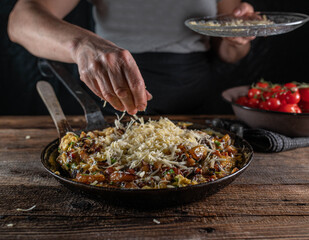 Woman sprinkles cheese over a pan with farmers breakfast. 