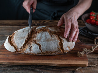 Cutting rustic  loaf of sourdough bread by womans hand with a bread knife