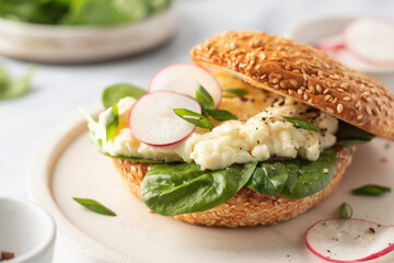 Breakfast burger with scrambled eggs, spinach, radish slices on white marble kitchen table. Close up