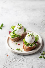 Poached egg sandwich with cucumber and microgreens. Healty breakfast bruschetta on light background. Keto diet, text space