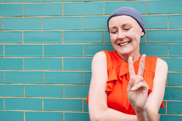 Smiling woman gesturing peace sign by brick wall