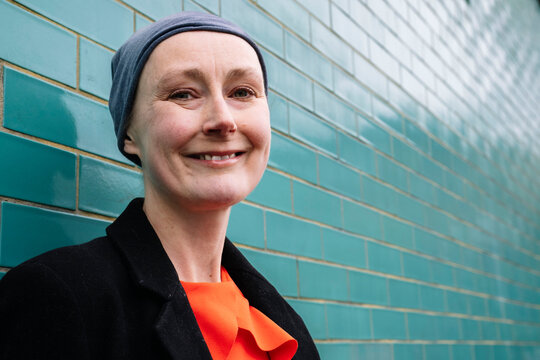 Smiling cancer patient wearing headscarf by brick wall