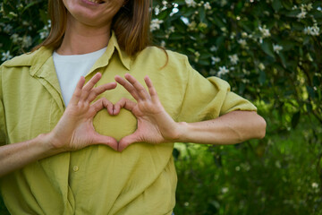 Woman making heart gesture on breast in garden