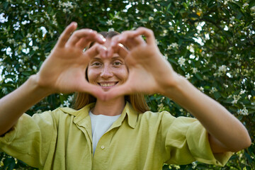 Smiling young woman making heart sign in garden
