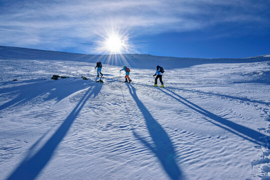 Austria, Tyrol, Sun shining over three skiers traveling through snow in Kitzbuehel Alps