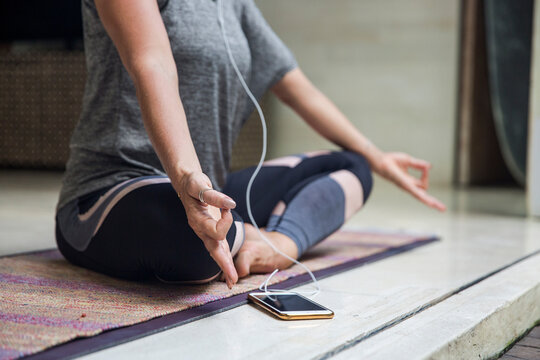 Woman practicing Lotus Position sitting cross-legged by smart phone at home