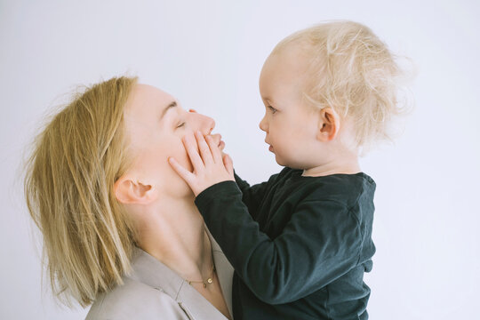 Son Touching Face Of Mother Puckering Against White Background