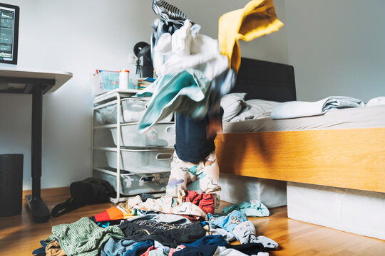 Toddler boy playing with cluttered clothes in bedroom at home