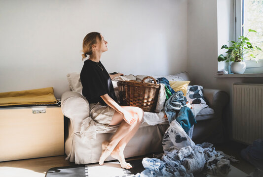 Thoughtful woman sitting on sofa with cluttered laundry at home