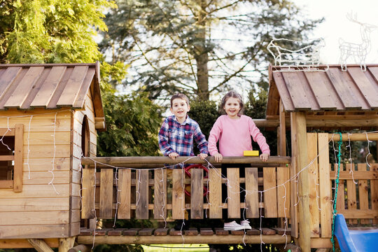 Siblings standing on wooden footbridge by playhouse in back yard