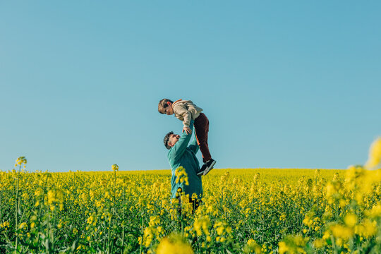 Father lifting son standing amidst flowers in rapeseed field