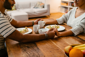 Close up of couple holding hands and praying during lunch while sitting in kitchen