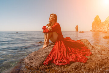 woman sea red dress. Beautiful sensual woman in a flying red dress and long hair, sitting on a rock...