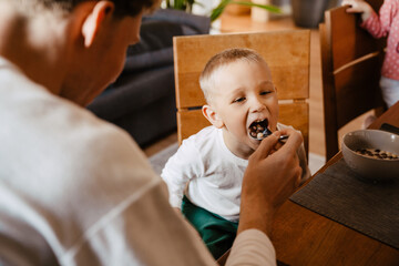 Father feeding his son with flakes while sitting in kitchen