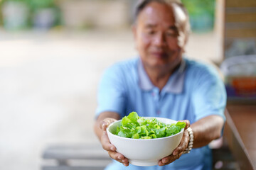 Thai man holding a white bowl with lettuce.