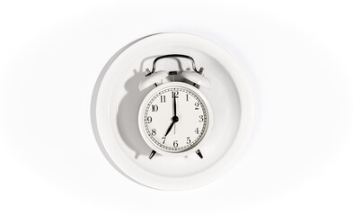 White alarm clock on a white plate on a white background, top view.