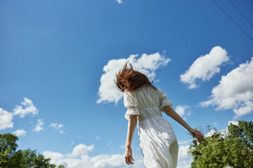a woman in a light dress against a blue sky stands with her back to the camera. Photo from below