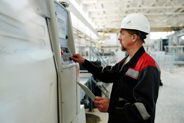 Engineer in uniform and hardhat setting the work of machine using digital tablet
