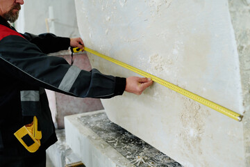 Close-up of worker measuring the big piece of stone with ruler while working in plant