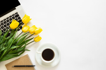 Laptop, a cup of coffee and a bouquet of tulips on a white background, top view.