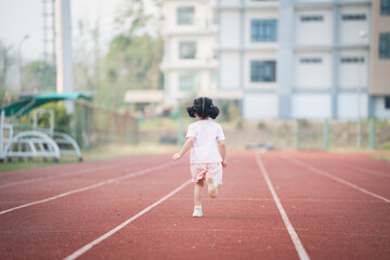 Baby asian girl run jogging at running track, run field at stadium. cute female exercise at sunset...