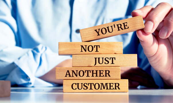 Naklejki Close up on businessman holding a wooden block with the "You're not just another customer" message